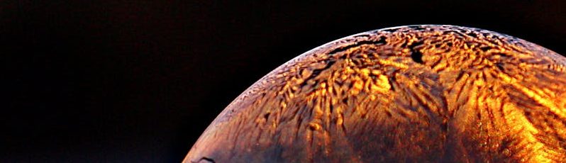 Close-up shot of a frozen bubble with warm reflections resting on a snowy surface at twilight.
